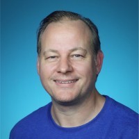 Aaron Eden facing the camera in a head-and-shoulders portrait on a blue background
