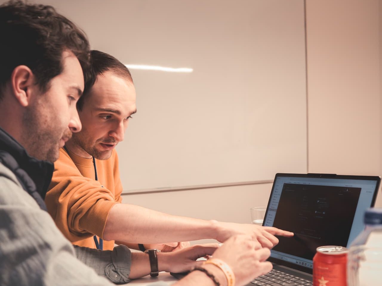 Two people at a desk reviewing a laptop screen, one pointing at the display