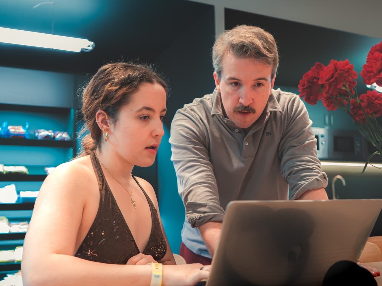 A seated person working on a laptop while a colleague leans in over the same screen